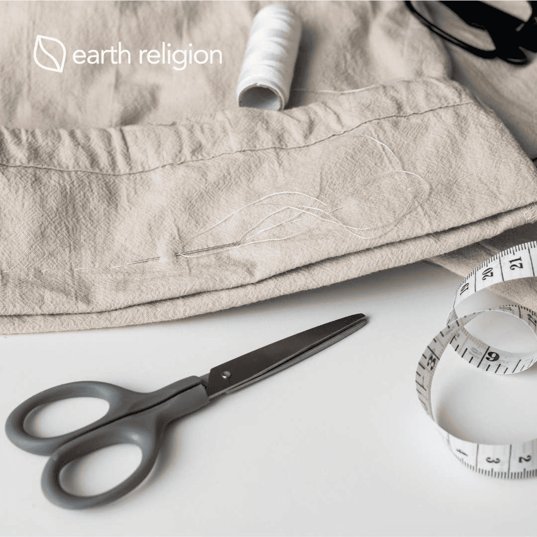 Thread, clothing, scissors, and a measuring tape on a craft table.